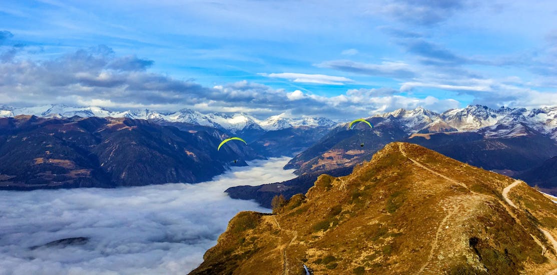 Two paragliders from Tandemflights Kronplatz are gliding over the beautiful mountain scenery around Plan de Corones and the Puster Valley.