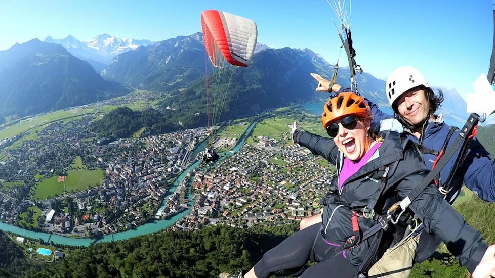 On a paragliding flight in Interlaken with Twin Paragliding, a certified tandem pilot and his passenger are taking a picture while gliding over the beautiful town of Interlaken.
