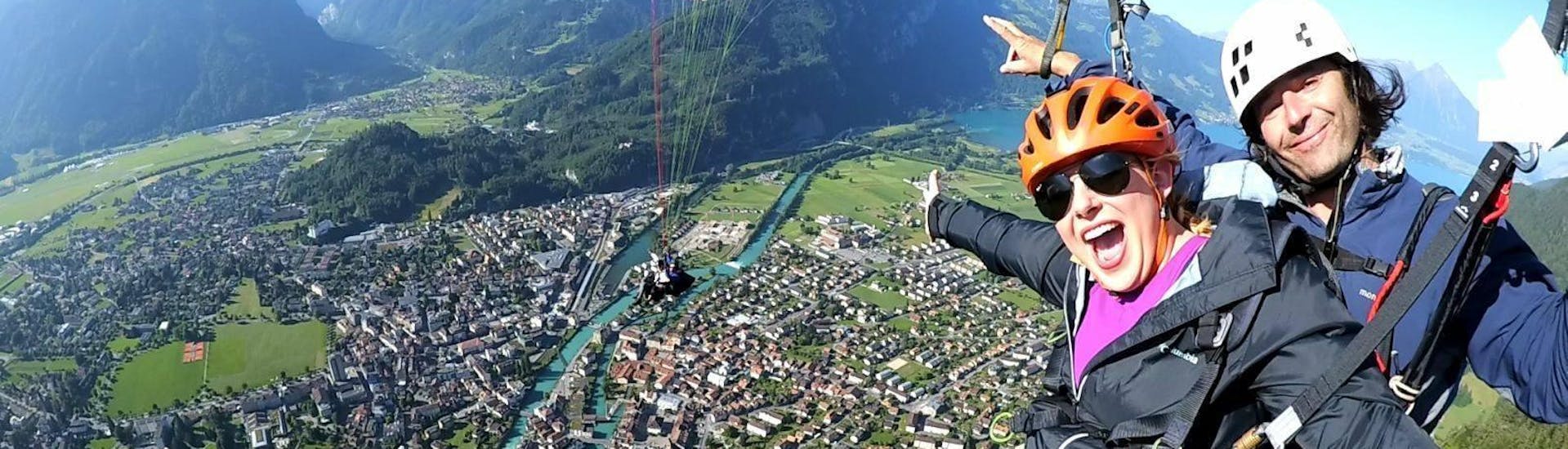 On a paragliding flight in Interlaken with Twin Paragliding, a certified tandem pilot and his passenger are taking a picture while gliding over the beautiful town of Interlaken.