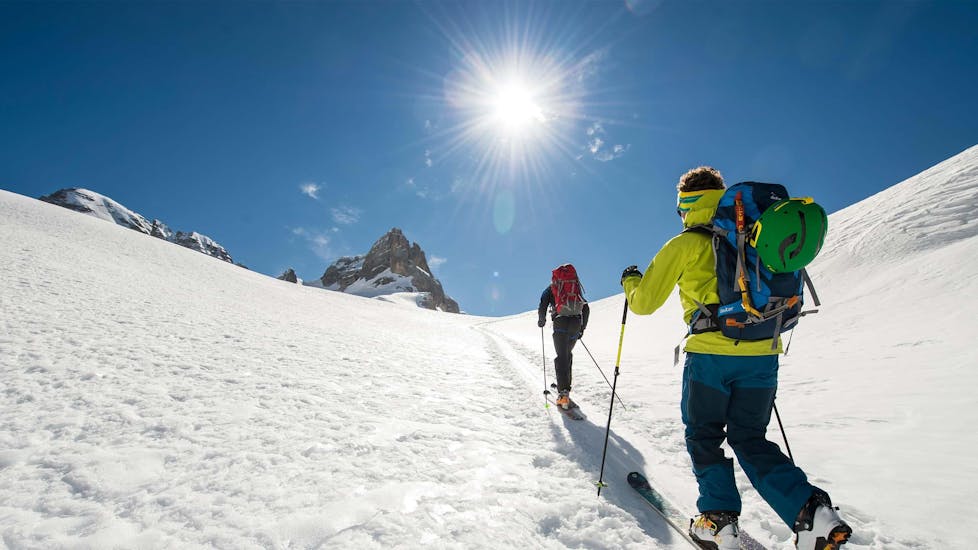 Zwei Skifahrer erklimmen bei ihrer Aktivität "Private Skitour für alle Levels" mit dem Anbieter Privatskischule Höll den Gipfel eines Berges.