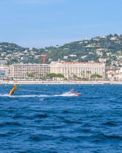 Un bateau à moteur traverse à toute vitesse les eaux bleues claires de la Côte d'Azure tout tirant un crazy sofa, une des différentes activités nautiques que l'on peut pratiquer à Nice.