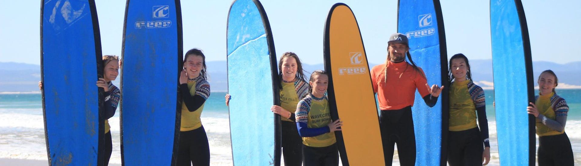 A group of happy surfers is taking a photo with their friendly surfing instructor from Wavecrest Surf School in Jeffreys Bay.