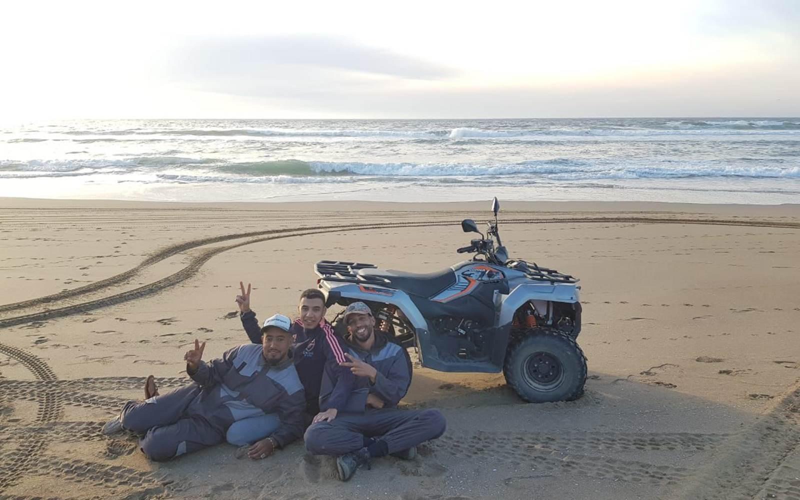 3 Hombres en la playa frente al quad de Galaxy Loisirs Agadir y el Océano Atlántico detrás