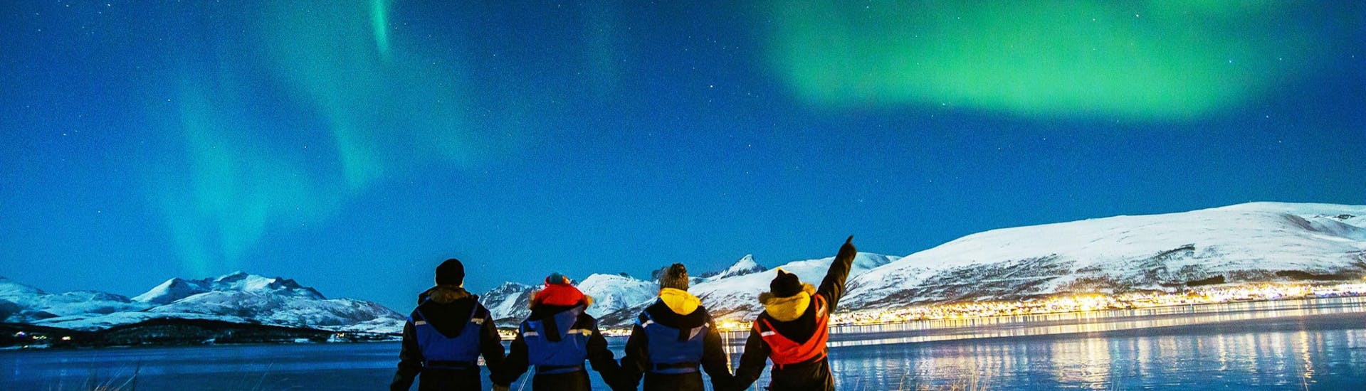 Eine Gruppe von Menschen blickt in den Himmel und bewundert die Nordlichter über Tromsø.