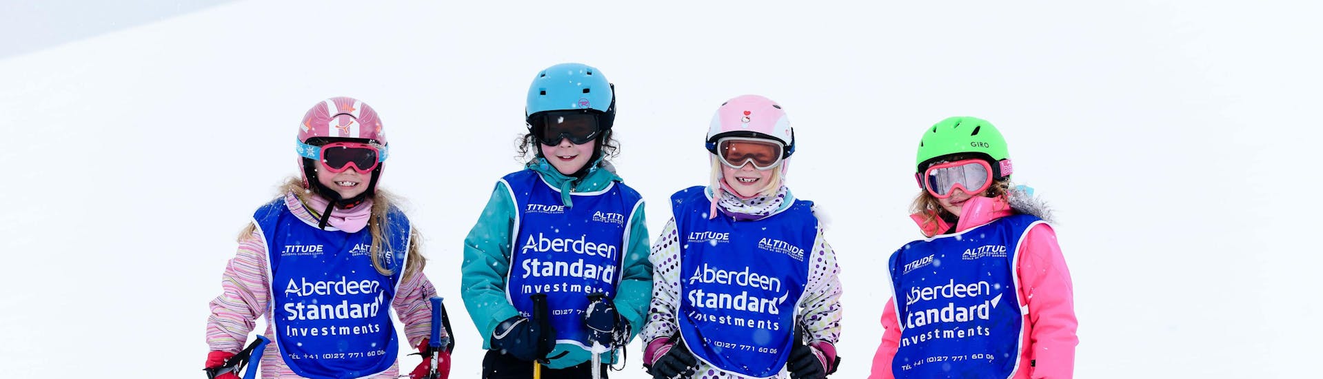 Four kids standing in a row with helmets and vests on during their kids ski lessons for all levels with skischule Altitude in Grindelwald and Wengen.