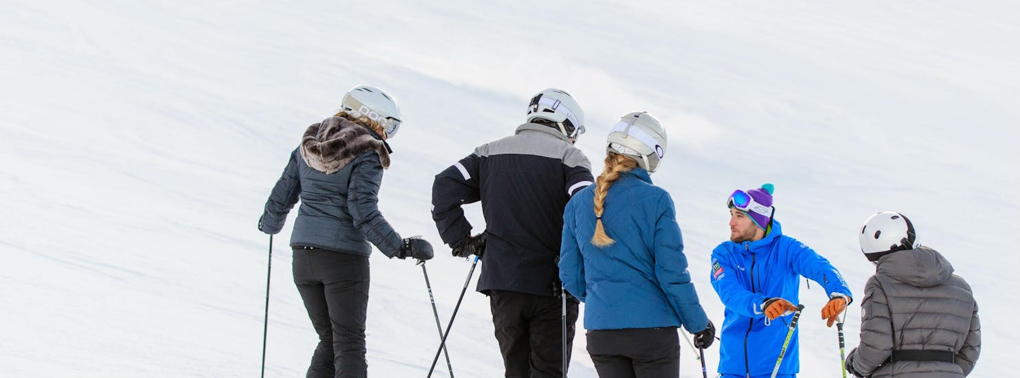 Three adults standing with their back to the camera facing their instructor on the slopes during their adult ski lessons for all levels with skischule Altitude in Grindelwald en Wengen.