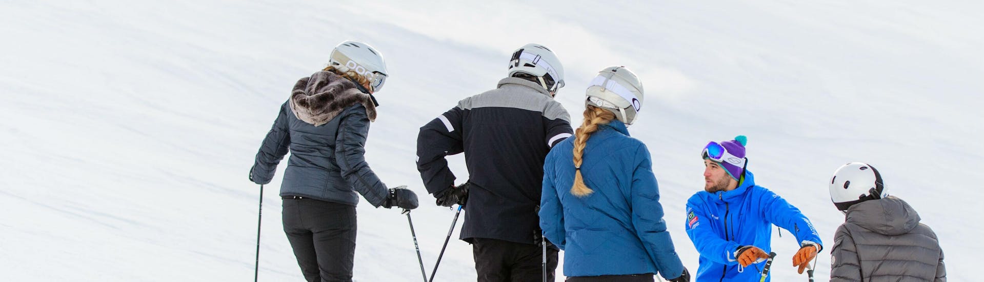 Three adults standing with their back to the camera facing their instructor on the slopes during their adult ski lessons for all levels with skischule Altitude in Grindelwald en Wengen.