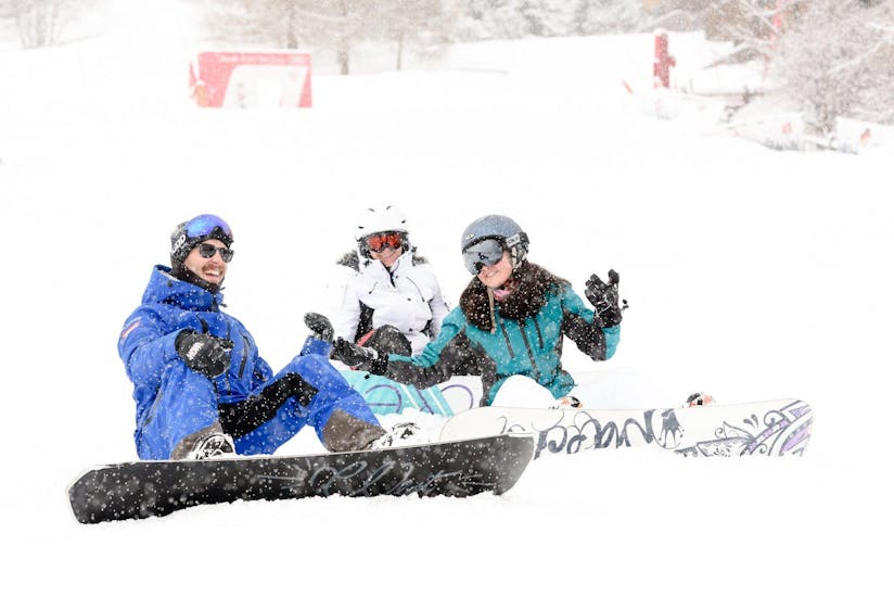 Drei Snowboarder sitzen im Schnee während ihres Snowboardkurses für Kinder und Erwachsene für alle Niveaus mit der Skischule Altitude in Grindelwald und Wengen.