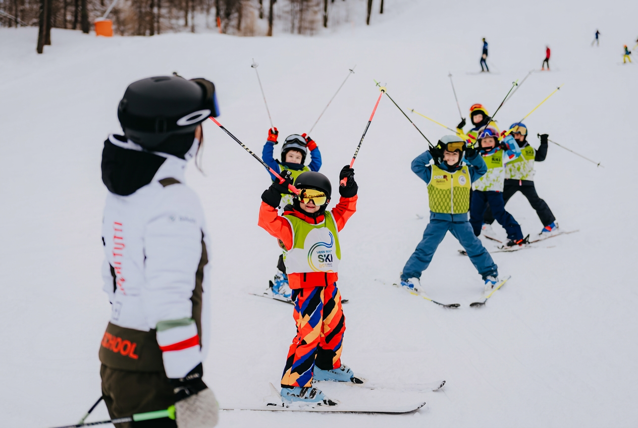 Un moniteur de ski enseigne à un groupe de jeunes enfants tenant leurs bâtons sur une pente enneigée lors de cours de ski pour enfants débutants (3-15 ans) avec l'école de ski Liberi Tutti.