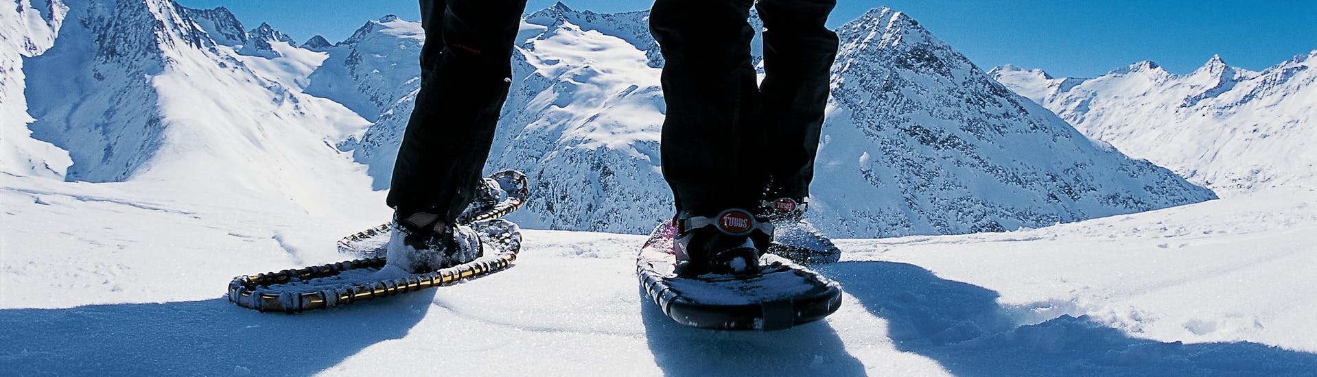 two persons wearing snowshoes are on top of a mountain during their snowshoeing tour for all levels with skischule Obergurgl.