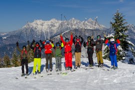 The skiers stand together with the ski instructor on the mountain and smile into the camera during the ski lessons for adults - beginner of the ski school S4 Snowsports Fieberbrunn.
