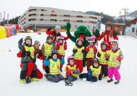 Die Kinder sitzen gemeinsam mit dem Maskottchen und dem Skilehrer der Skischule S4 Snowsports Fieberbrunn im Schnee und heben die Hände während dem Kinder Skikurs "Tatzis Skicircus" (3-14 Jahre) - Alle Levels.