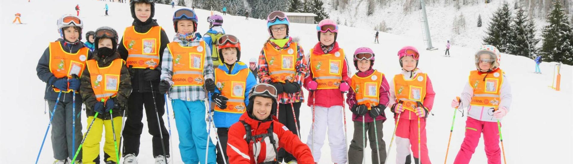 A group of children and their ski instructor from S4 Snowsport Fieberbrunn are smiling at the camera during their Kids Ski Lessons "Juniors programme" (15-18 years).