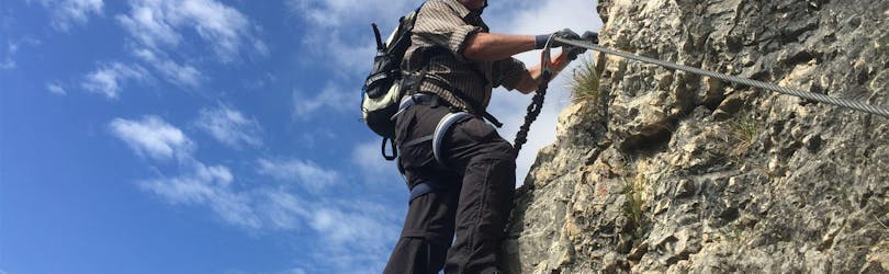 Ein furchtloser Teilnehmer erklimmt die Felswand während des Klettersteigs Monte Albano - Historischer Weg mit Bewegung - Into Nature Lago di Garda.