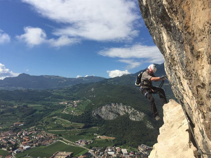 A participant is climbing down a rock face with an amazing view during the Via Ferrata Monte Albano - Historical Route with Mmove - Into Nature Lago di Garda.