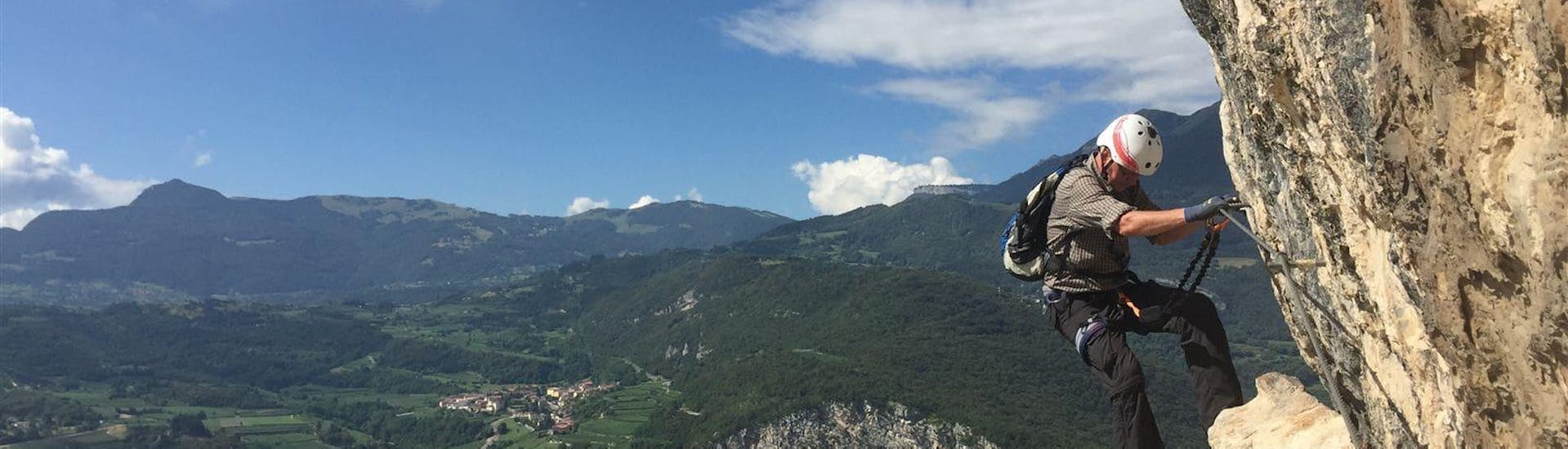 Un participant descend une paroi rocheuse avec une vue imprenable pendant la Via Ferrata Monte Albano - Itinéraire historique avec Mmove - Into Nature Lago di Garda.