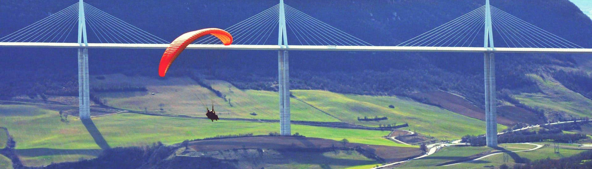 A paragliding pilot from Air Magic Parapente is doing a Tandem Paragliding Flight "Discovery Kids" in front of the Millau Viaduct.