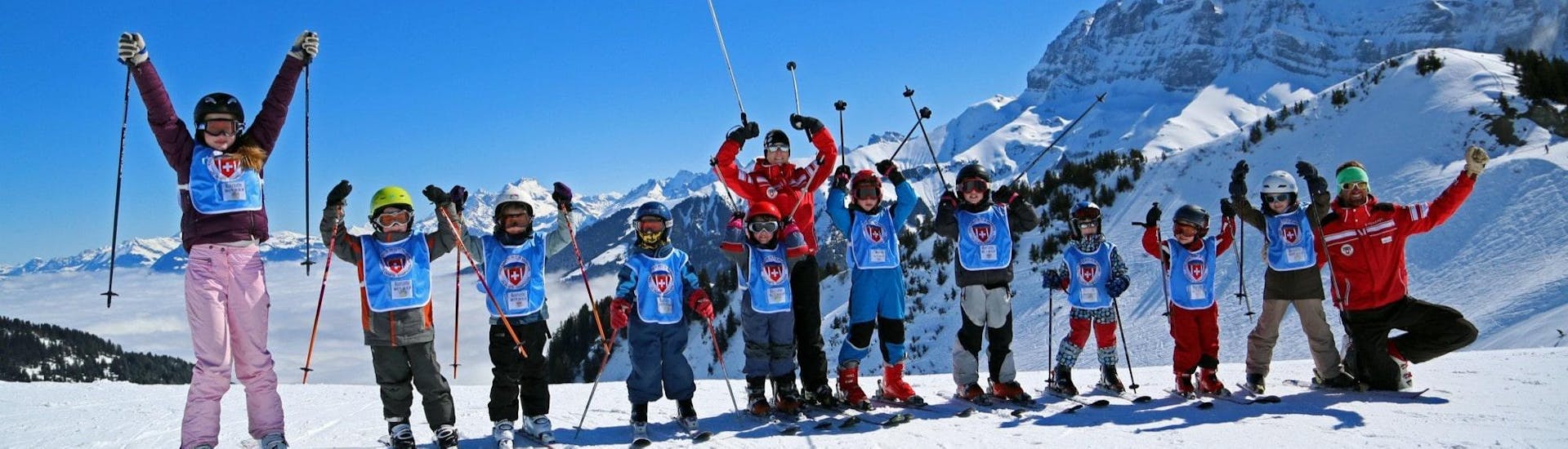 Des enfants se tiennent les uns à côté des autres avec leurs bâtons en l'air avant leur Cours de ski pour Enfants (dès 4 ans) - Tous niveaux avec l'École Suisse de Ski Crosets-Champoussin.