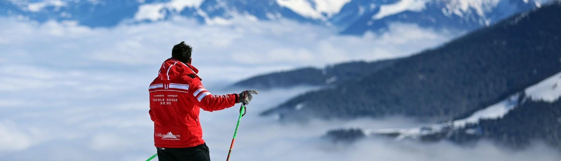 A ski instructor from the Swiss Ski School Les Crosets-Champoussin is standing at the top of a mountain during a Private Ski Lessons for Adults - All Levels.