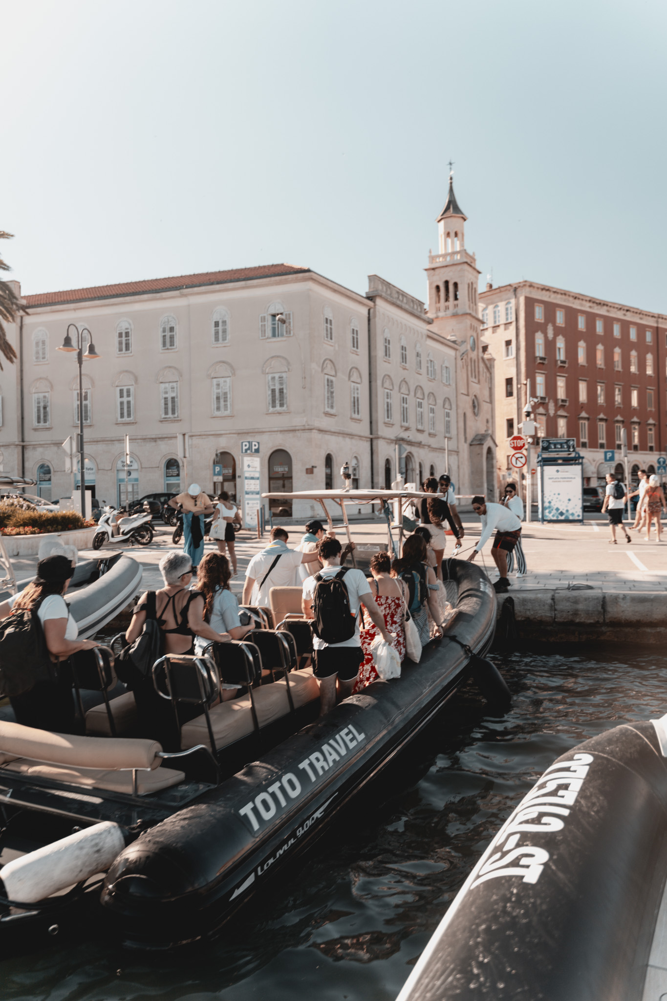 Een groep toeristen stapt aan boord van een zwarte Toto Travel Split-rubberboot in de zonnige haven van Split, klaar voor hun boottocht langs de 6 eilanden, waaronder de Blauwe Grot en Hvar.