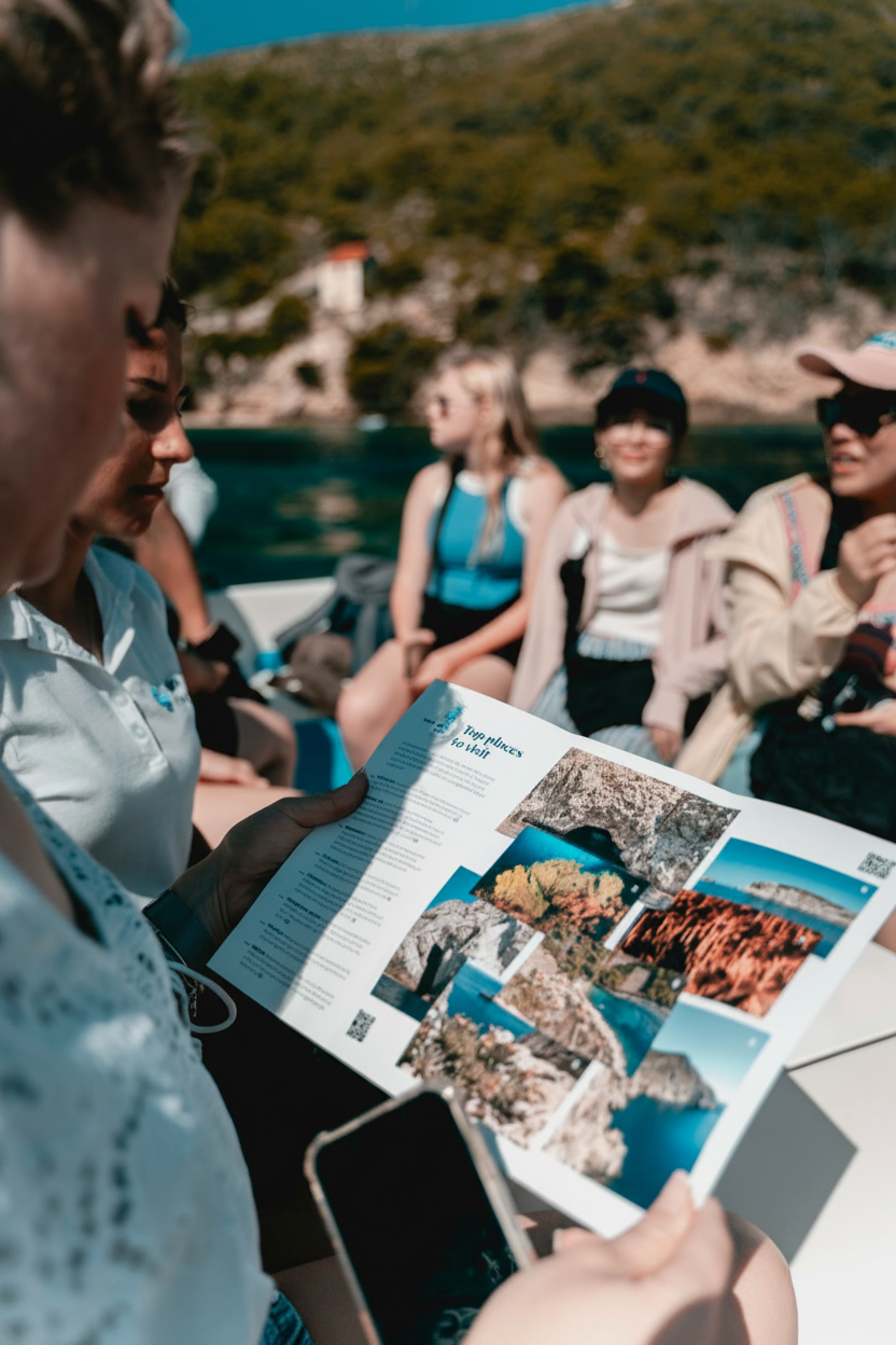 Un groupe de jeunes, participant à une excursion en bateau vers les 6 îles au départ de Split organisée par Toto Travel Split, consulte une brochure présentant des photos de la Grotte Bleue et de Hvar.