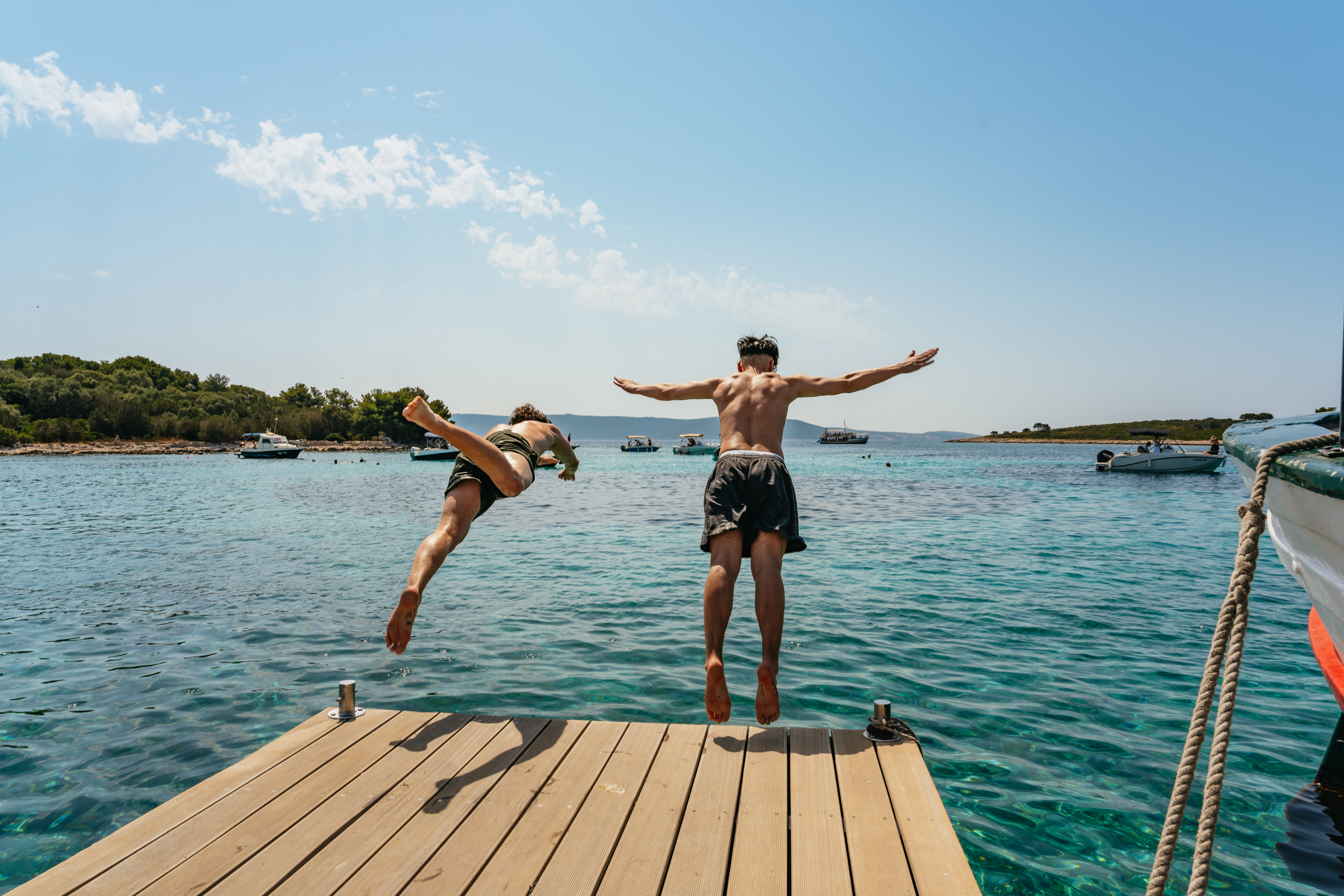 Two men jump from a wooden dock into the clear blue sea during a 3 Islands and Blue Lagoon Boat Trip from Split with Toto Travel Split.