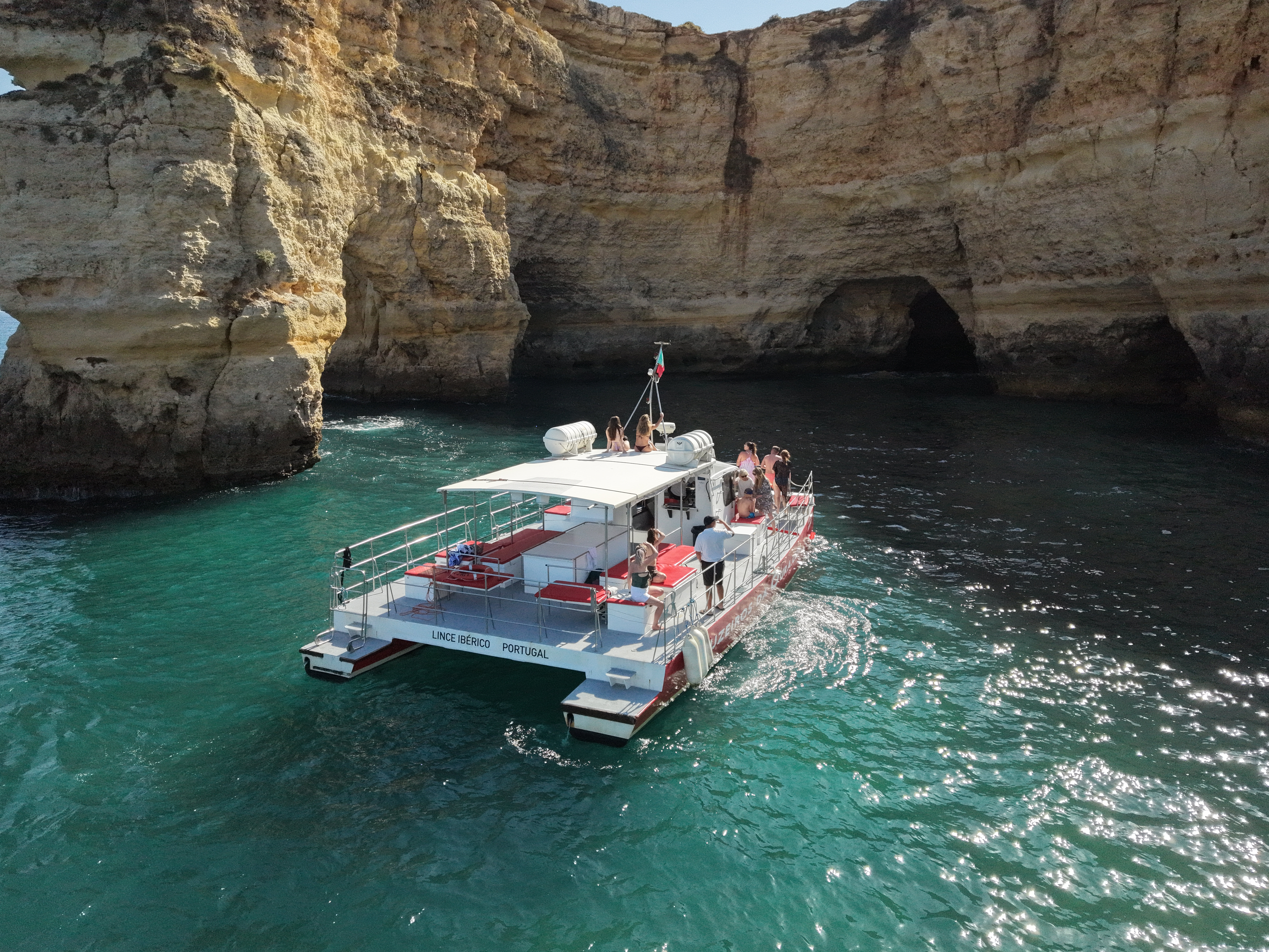 Il catamarano AlgarExperience naviga sulle acque turchesi costeggiando le splendide scogliere durante un'escursione in barca alle grotte e alla costa di Benagil, con partenza da Vilamoura.