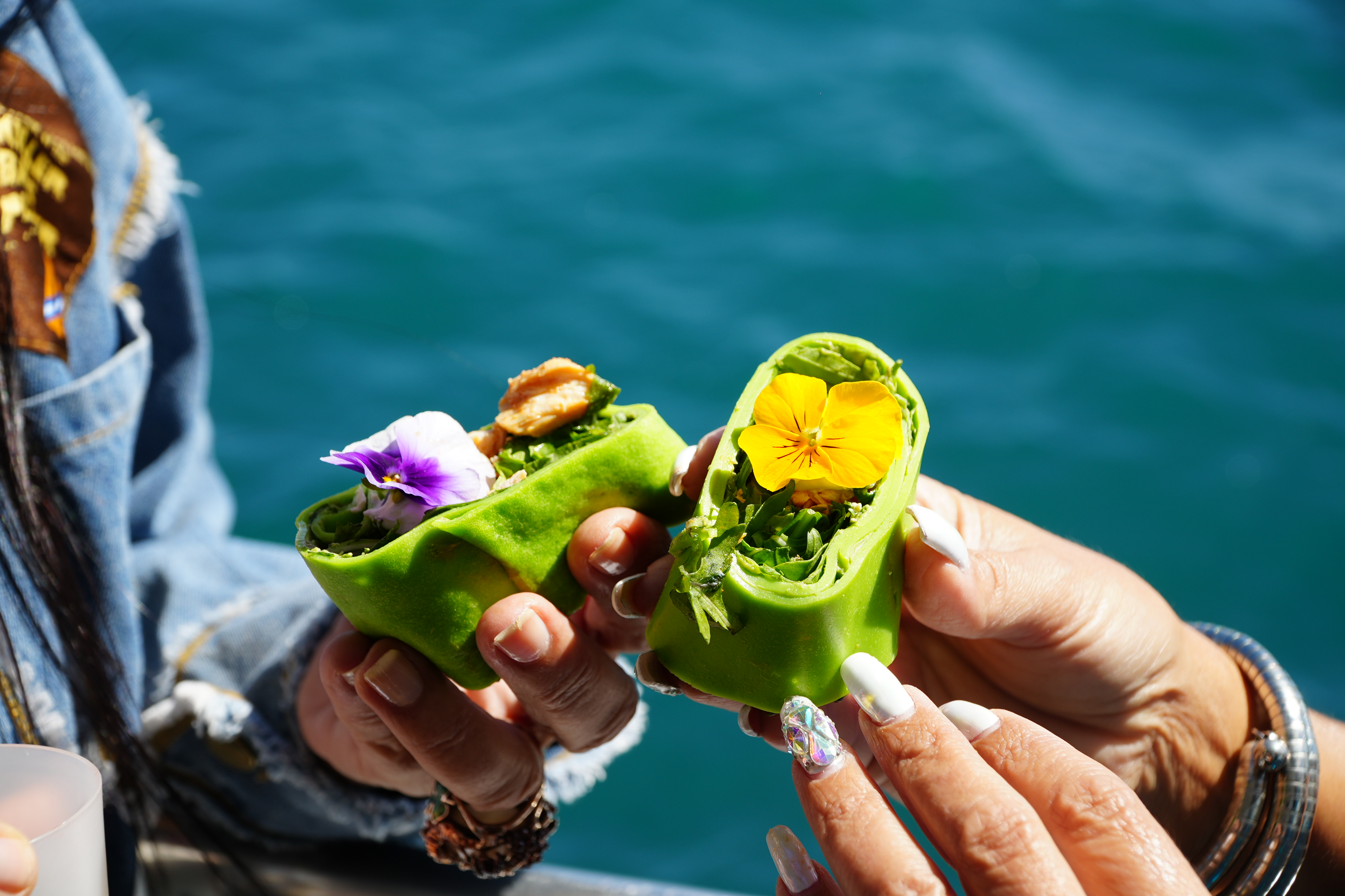 A guest holds up two green wraps with edible flowers from the brunch on board during the Vilamoura Boat Trip by AlgarExperience.