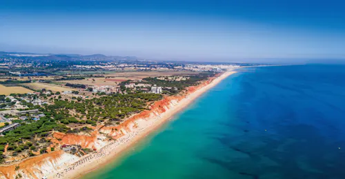 Scogliere rosse e spiaggia sabbiosa sulla costa di Vilamoura Vista aerea della splendida costa di Vilamoura con le sue scogliere rosse e le spiagge dorate, uno dei punti salienti del tour Brunch & Benagil Caves with Open Bar di AlgarExperience.