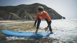 Ein Kind auf einem Surfbrett während des Surfunterrichts (ab 6 J.) am Praia Castelejo mit der Good Feeling Surf School Algarve.