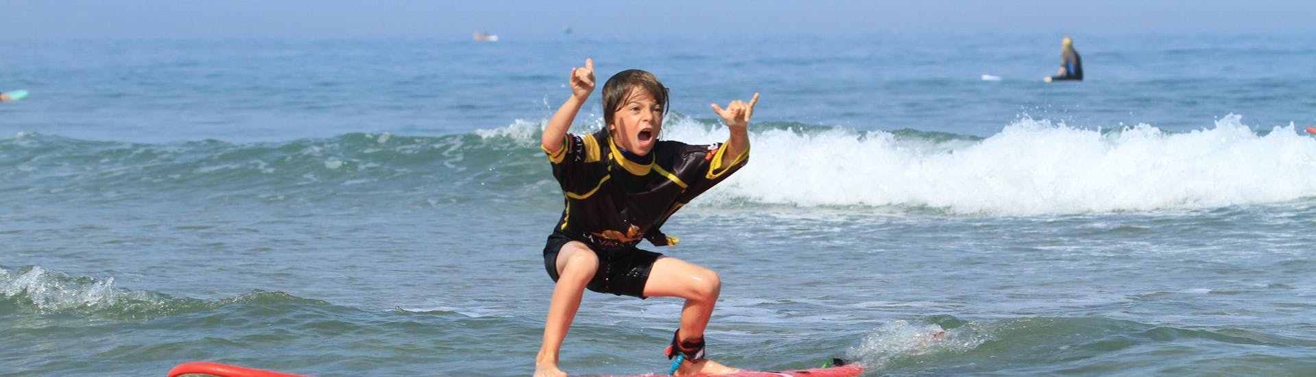 Een kind staat trots op zijn surfplank dankzij de surflessen voor kinderen op het strand van de Côte des Basques met La Vague Basque.
