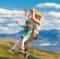 Ein erfahrener Guide von Edison Zipline Krk gleitet während der Zipline Tour „Entdecke Krk“ auf der Insel Krk in Kroatien gemeinsam mit einem jungen Mädchen entlang einer Seilrutsche.