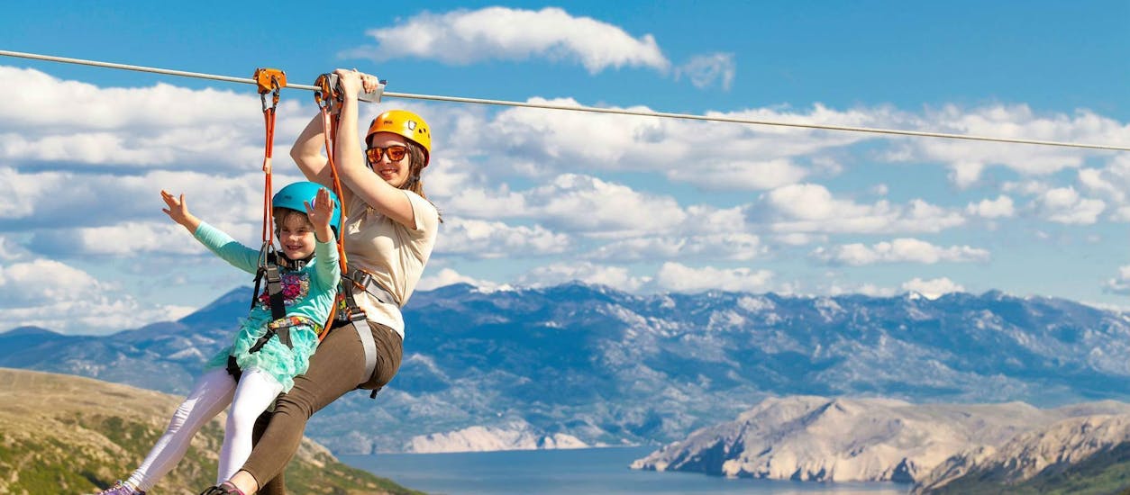 A small happy girl is gliding on a zipline with a qualified guide from Edison Zipline Krk during the zipline tour "Explore Krk“ on the Island of Krk.