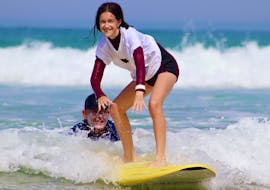 A girl learns how to surf during her Surf Lessons for Kids (4-10 y.) on Lacanau Centrale Beach with Hurley Surf Club Lacanau.