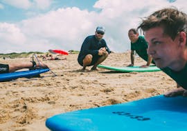 Un moniteur de surf de l'école de surf ESCF Anglet - Seignoss donne des instructions sur le sable aux participants d'un cours privé de surf sur la plage des Bourdaines.