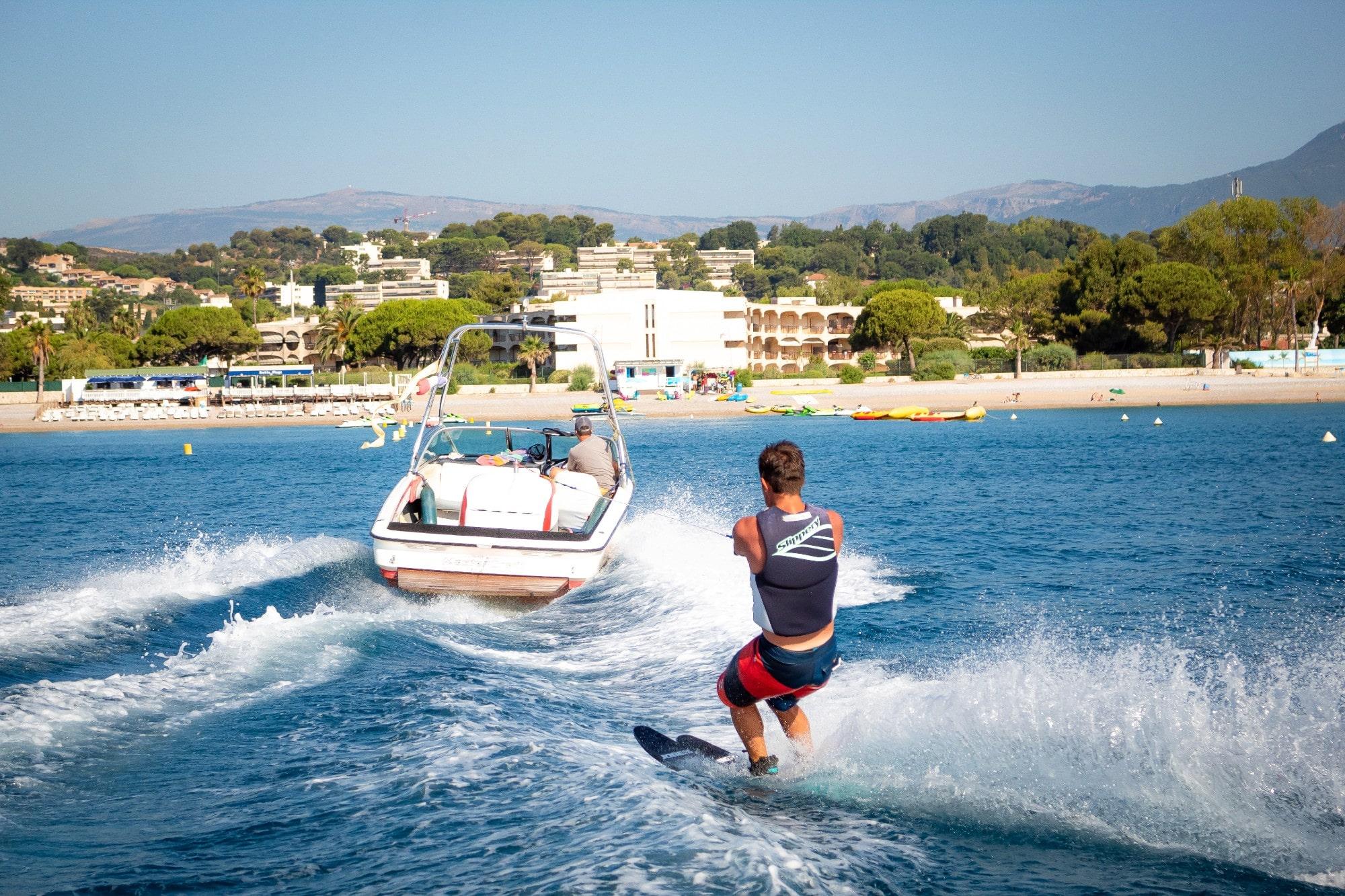 A man is being towed by a boat while Waterskiing in Cagnes-sur-Mer with Plage des Marines.