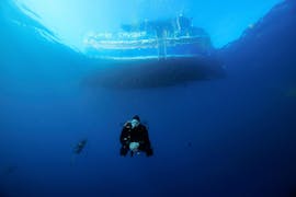 Un participant au Cours de Plongée pour Débutants - SSI Open Water Diver avec Octopus Garden à Malte plonge dans l'eau bleu sous un bateau.