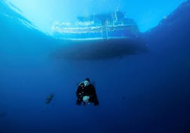 Een deelnemer aan de Scuba Duikcursus voor Beginners - SSI Open Water Diver met Octopus Garden duikt onder een boot in de blauwe oceaan rond Malta.