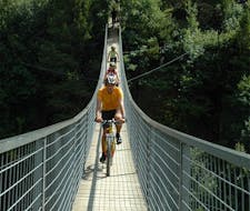 Three cyclists are crossing a bridge during their Mountain Bike Tour on the Ötztal Trail with CanKick Ötztal.