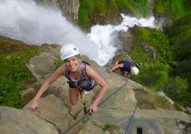 Eine Frau und ein Mann klettern bei einem Klettersteig im Ötztal - "Wasserfall" mit CanKick-Ötztal eine Felswand am Rande eines Wasserfalls hinauf.