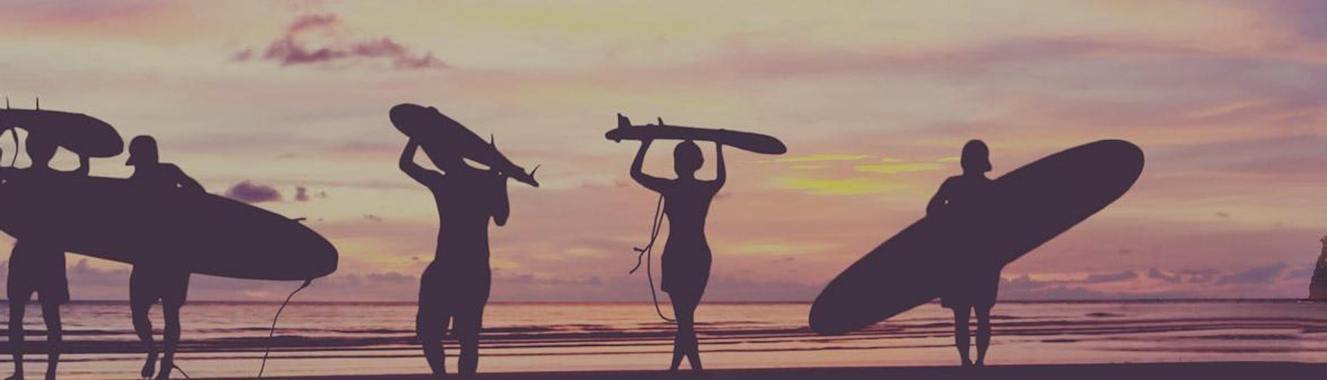 Surfers lopen op het strand bij zonsondergang met hun surfplank op hun hoofd of onder hun arm aan het einde van hun surflessen op het strand van Hendaye tijdens het hoogseizoen met de surfschool École de surf Hendaia