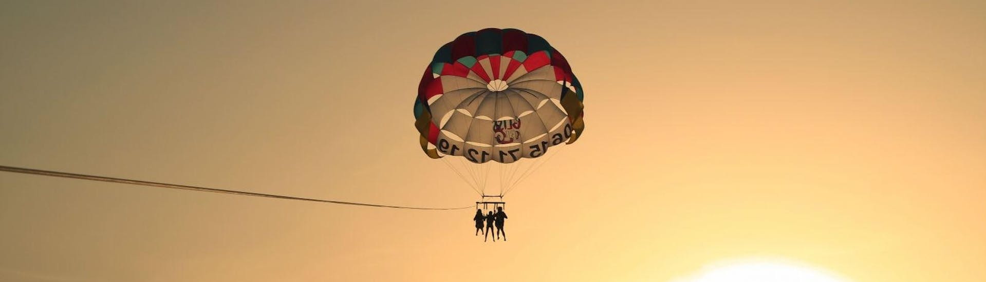 Three people from the watersports company Gliss1Flo parasailing during sunset in Saint-Florent with a view of the coast of North Corsica. 