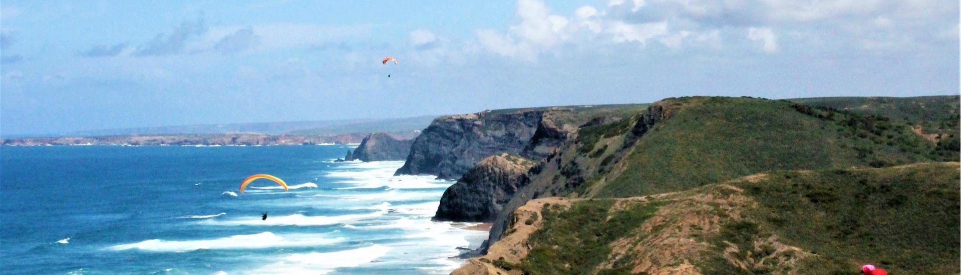 Zwei Gleitschirmflieger schweben hoch über dem Strand, an dem Flytrip  sein Tandem Paragliding - Praia da Cordoama anbietet