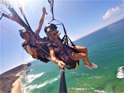Ein Tandempilot und sein Passagier gleiten beim von Flytrip organisierten Tandem Paragliding an der Praia da Cordoama über das türkisfarbene Wasser des Atlantiks.