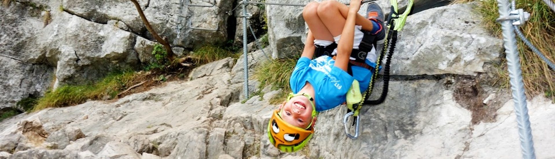 Kid smiling while hanging upside down during the Via Ferrata on Monte Colodri for Adults and Kids with SKYclimber Tremosine