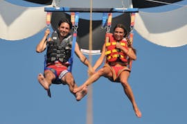 Un couple sourit dans le ciel pendant le parachute ascensionnel sur la plage de Perissa ou Perivolos à Santorin avec Wavesports Santorini.