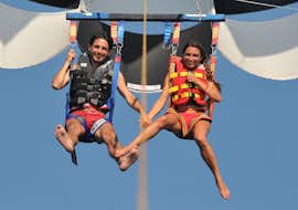 Parasailing sur les plages de Perissa ou Perivolos à Santorin avec Wavesports Santorini Un couple sourit dans le ciel pendant le parachute ascensionnel sur la plage de Perissa ou Perivolos à Santorin avec Wavesports Santorini.
