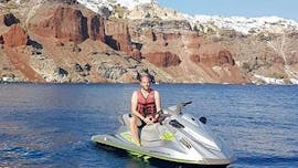 Durante un tour in moto d'acqua alla scoperta delle spiagge vulcaniche di Santorini condotto da una guida esperta di Crazy Sports, un turista posa per una foto con delle scogliere di origine vulcanica sullo sfondo.