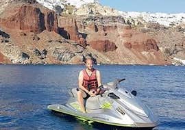 Jet Ski Safari to the Volcanic Beaches from Agios Georgios During a jet ski tour to volcanic beaches lead by an experienced guide from Crazy Sports, a tourist is posing for a photo with cliffs of volcanic origin in the background.