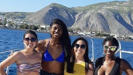 Durante il tour privato in barca "Scegli l'itinerario" da Agios Georgios organizzato da Crazy Sports, un gruppo di amici posa per una foto con gli spettacolari paesaggi vulcanici dell'isola sullo sfondo.